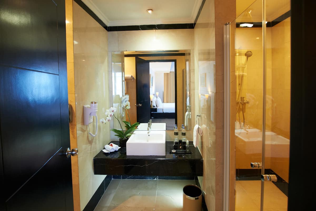 A modern bathroom with a large mirror, a sink, a shower, and a trash can.