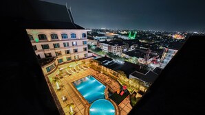A rooftop pool area with a large rectangular pool and a smaller circular pool, surrounded by potted plants and outdoor seating.