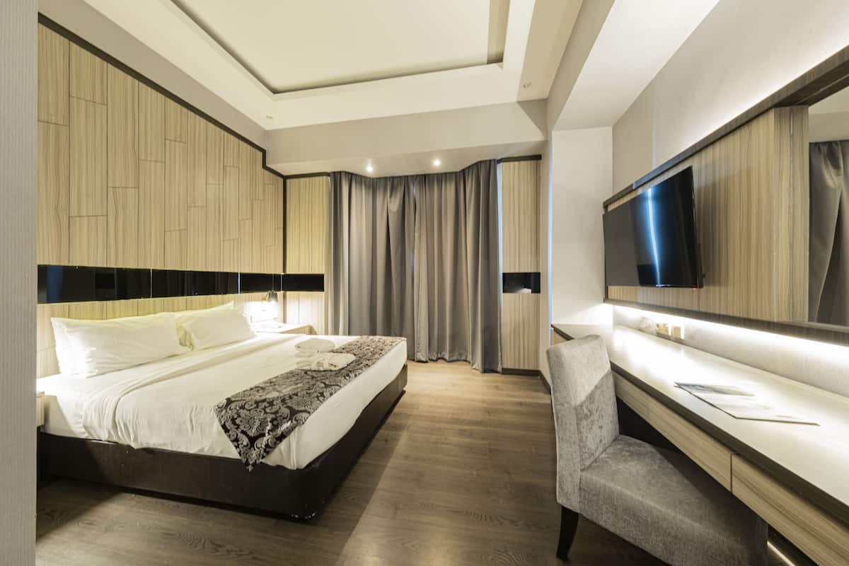 A modern hotel room with a large bed, a desk with a chair, a flat-screen TV, and a large mirror.