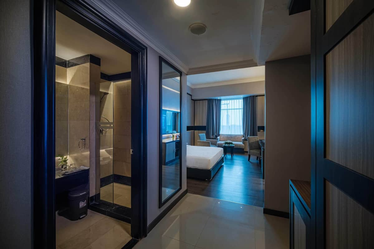 A hotel room with a glass shower, a bed, a sofa, and a dining area.