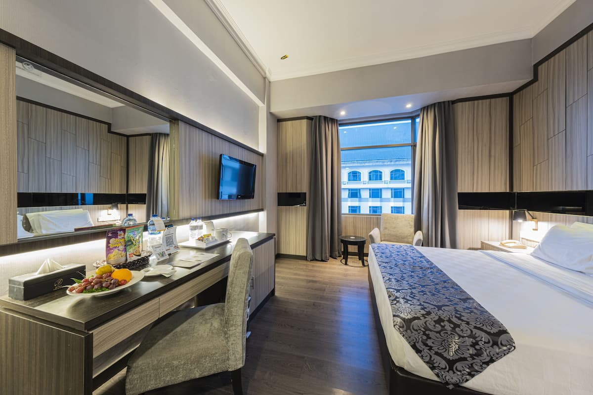 A modern hotel room with a large bed, a desk with a chair, a flat-screen TV, and a view of a building through the window.