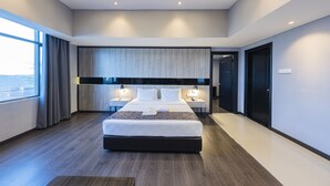 A modern hotel room with a large bed, bedside tables, a built-in headboard, and a view through a large window.