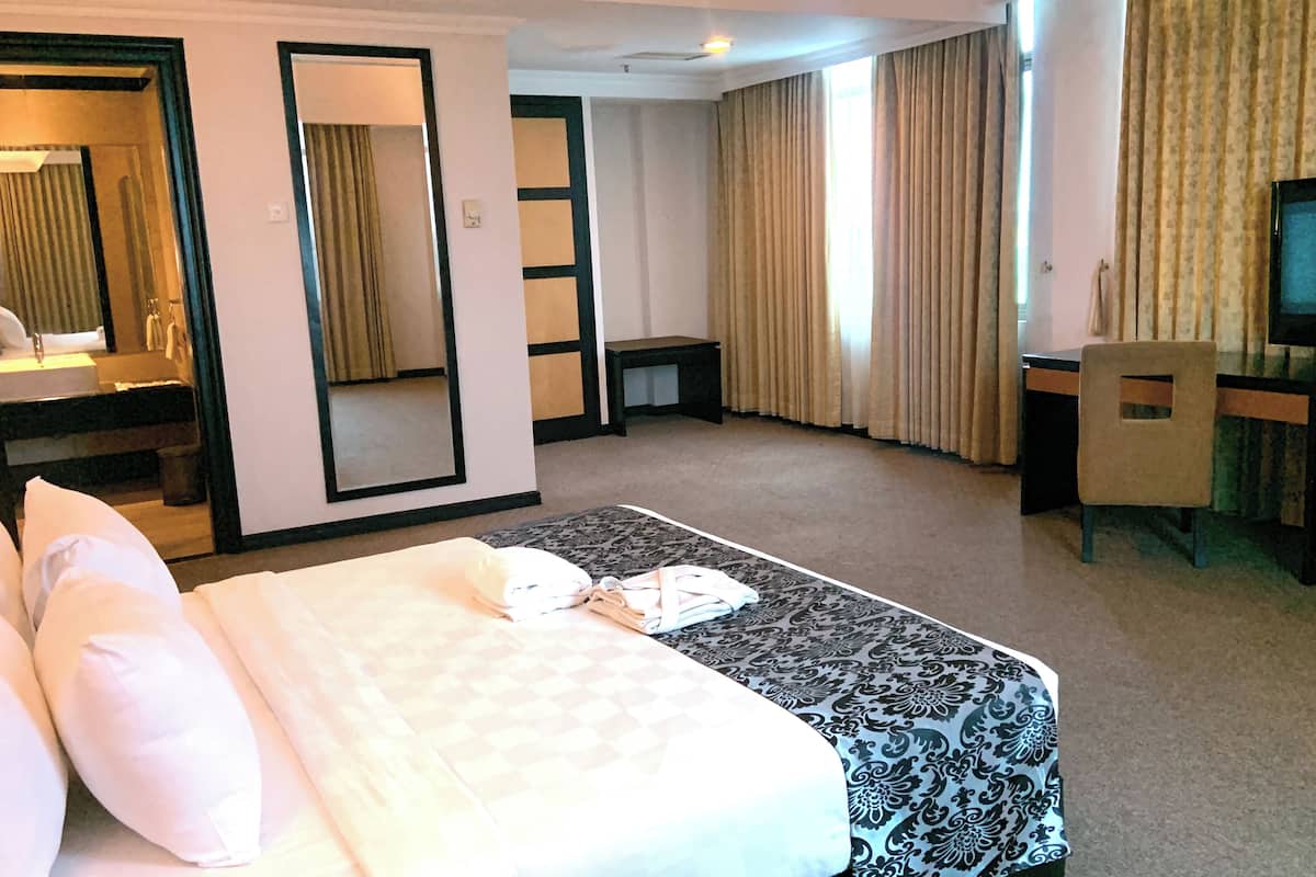 A hotel room with a bed, a desk, a television, and a bathroom visible through an open door.