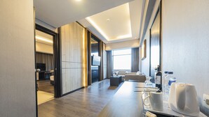 A modern hotel room with a wooden floor, a flat-screen TV, a sofa, and a coffee station.