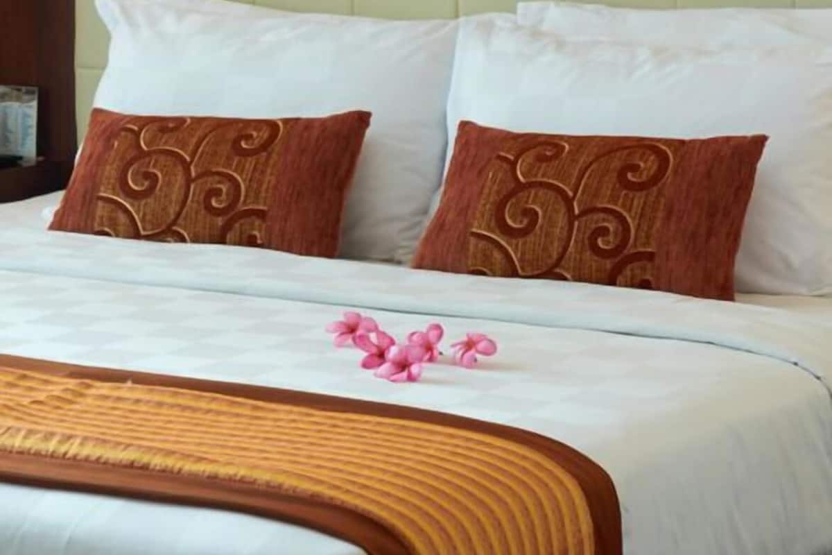 Una habitación de hotel con una cama, almohadas, una colcha y un cuadro en la pared.