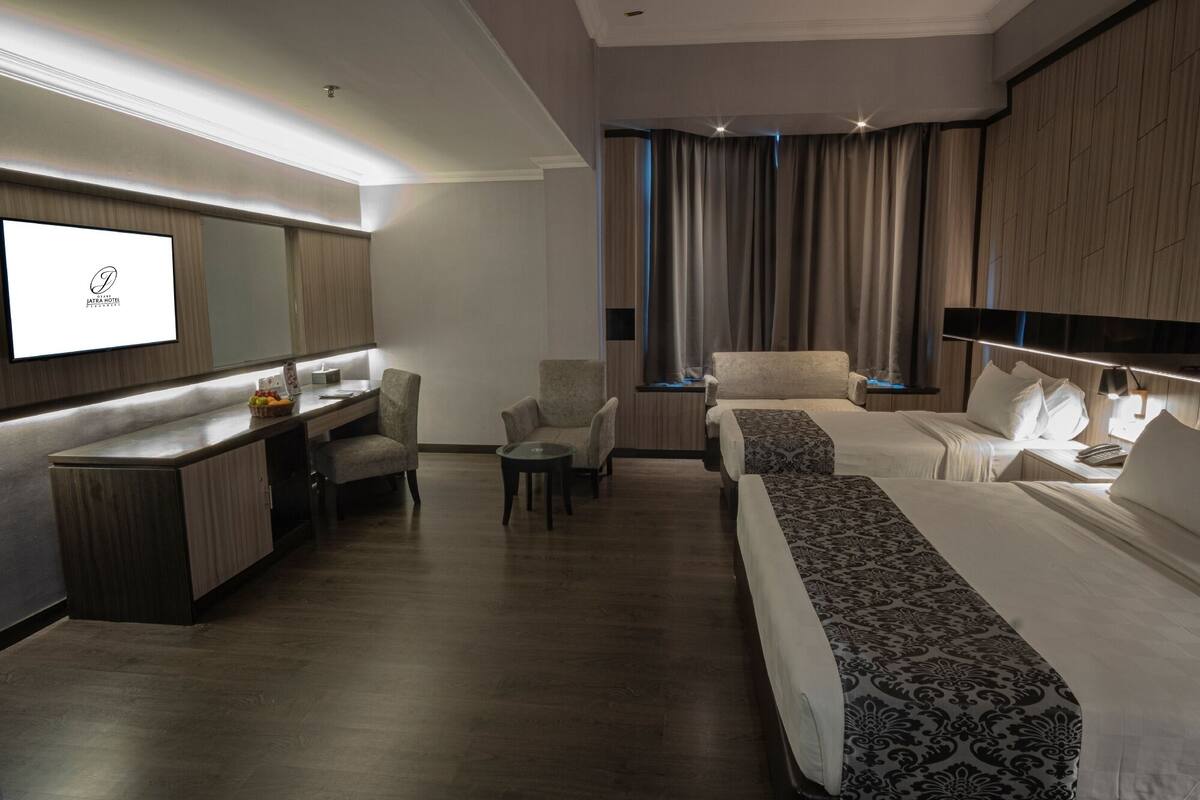 A hotel room with a desk, two chairs, a bed, a TV, and a large window with curtains.