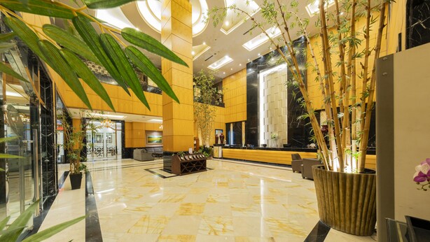 A modern lobby with a marble floor, reception desk, and potted plants.