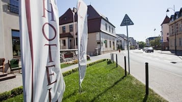Un hotel amb banderes a la vorera, un carrer amb cotxes i edificis al fons.