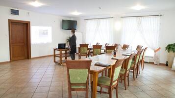 Un salón de conferencias con una larga mesa, sillas, un proyector y un televisor en la pared.