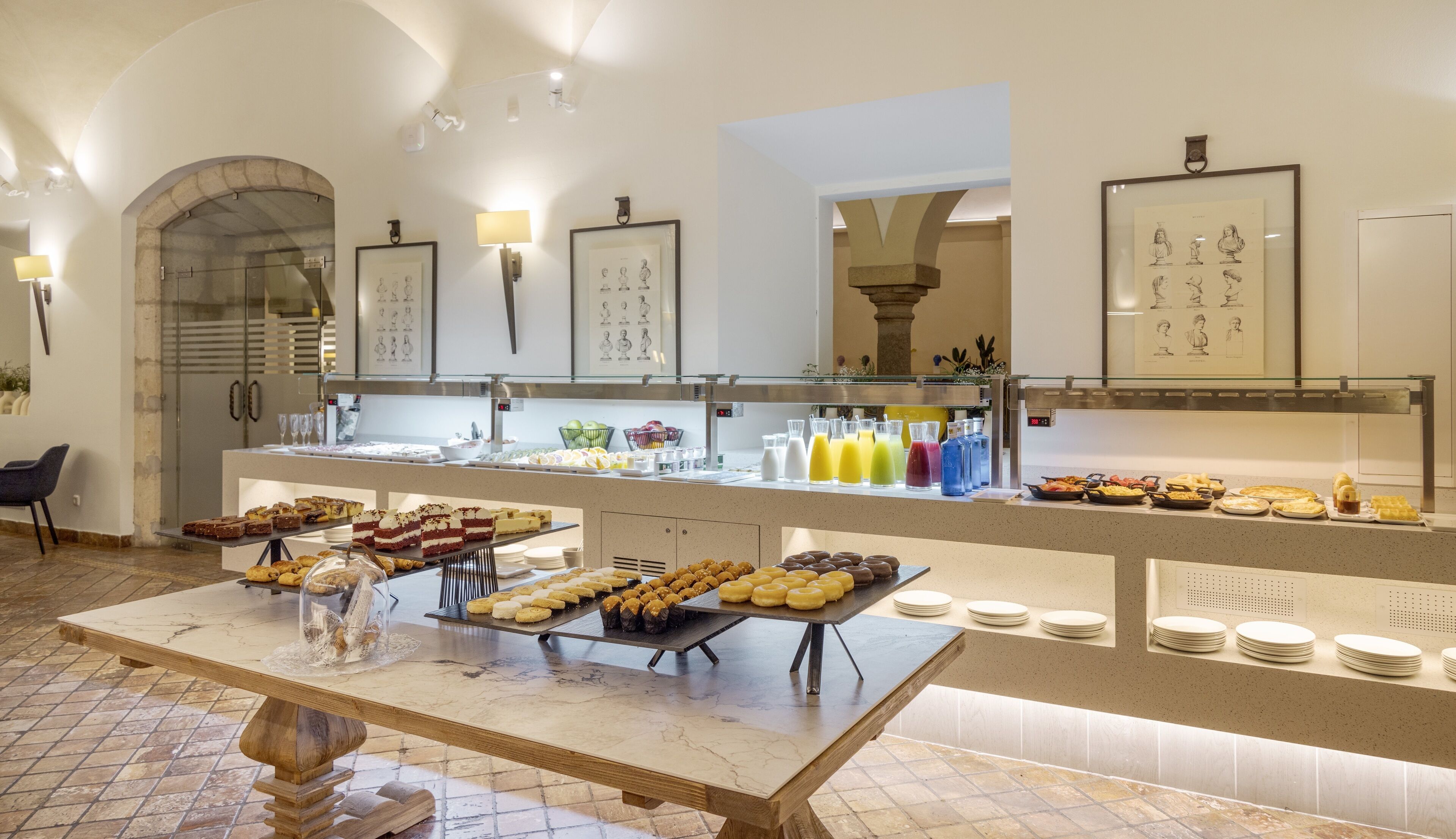 A buffet with various food items and beverages, a marble-tiled floor, and framed artwork on the walls.