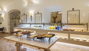 A buffet with various food items and beverages, a marble-tiled floor, and framed artwork on the walls.
