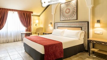 Hotelkamer met een groot bed, een rode plaid, een hoofdbord met een decoratief patroon, een klein rond tafeltje en een stoel.