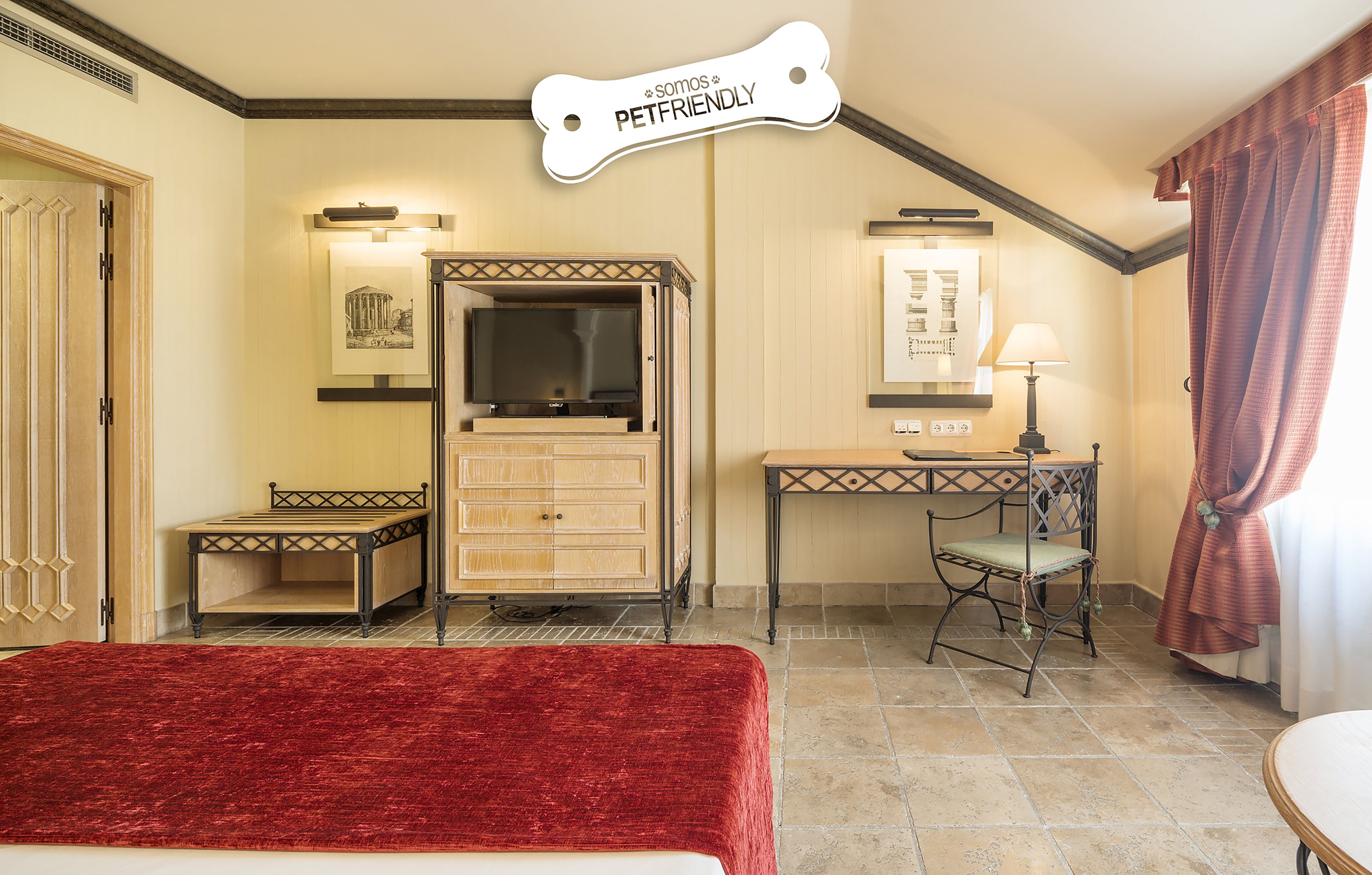 A hotel room with a bed, a desk, a chair, a television, and a pet-friendly sign.