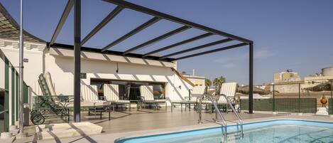 A rooftop pool area with a clear blue pool, lounge chairs, and a pergola structure.