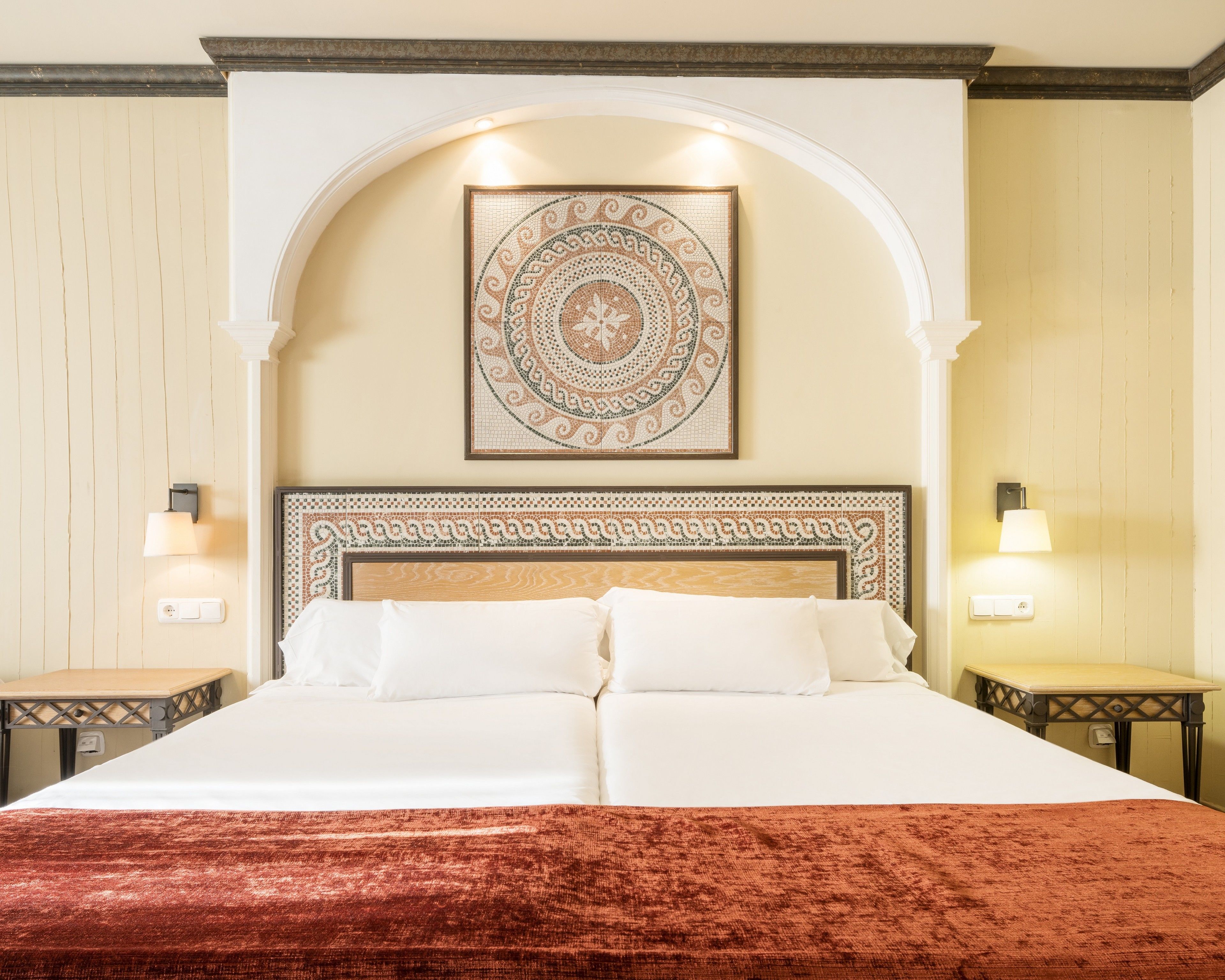 Una cama doble con un edredón rojo, un cabecero decorativo y una obra de arte de mosaico arriba.