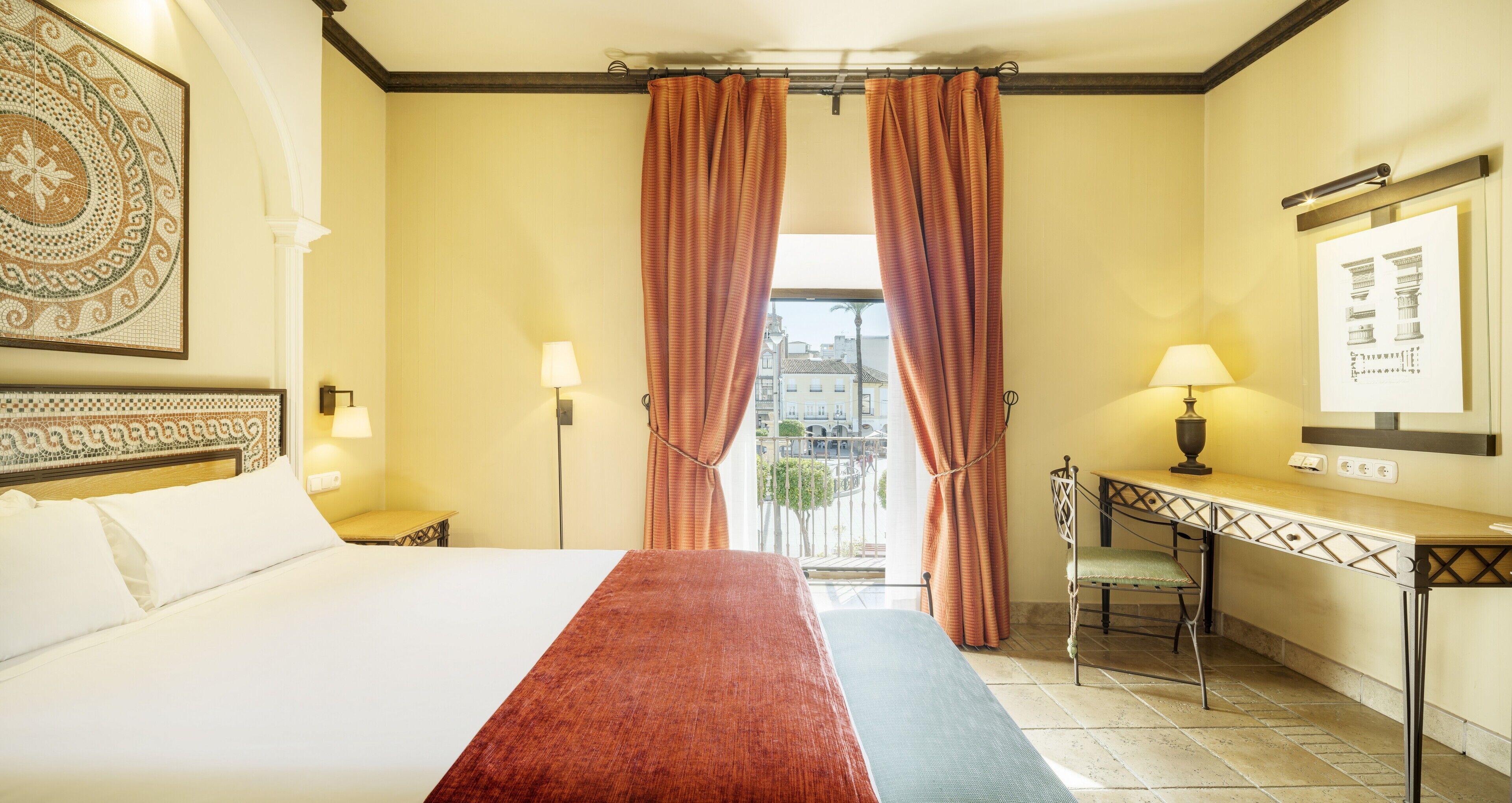 Una habitación de hotel con una cama grande, dos lámparas de noche, un escritorio con silla y vistas a la ciudad desde la ventana.