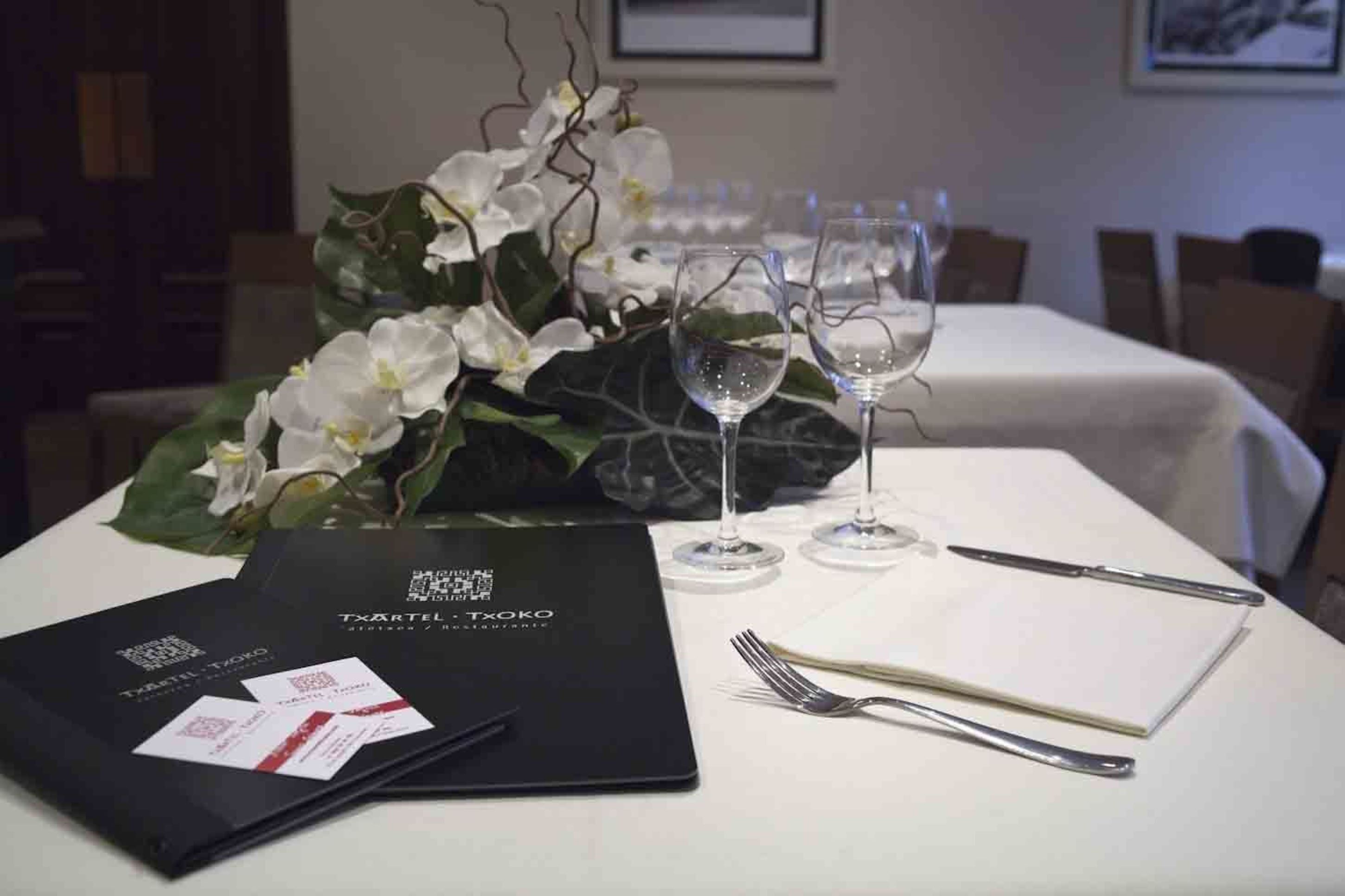 A dining table set with a menu, wine glasses, and cutlery.