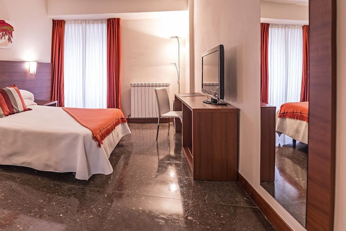 A hotel room with a bed, a desk, a TV, and a large mirror.