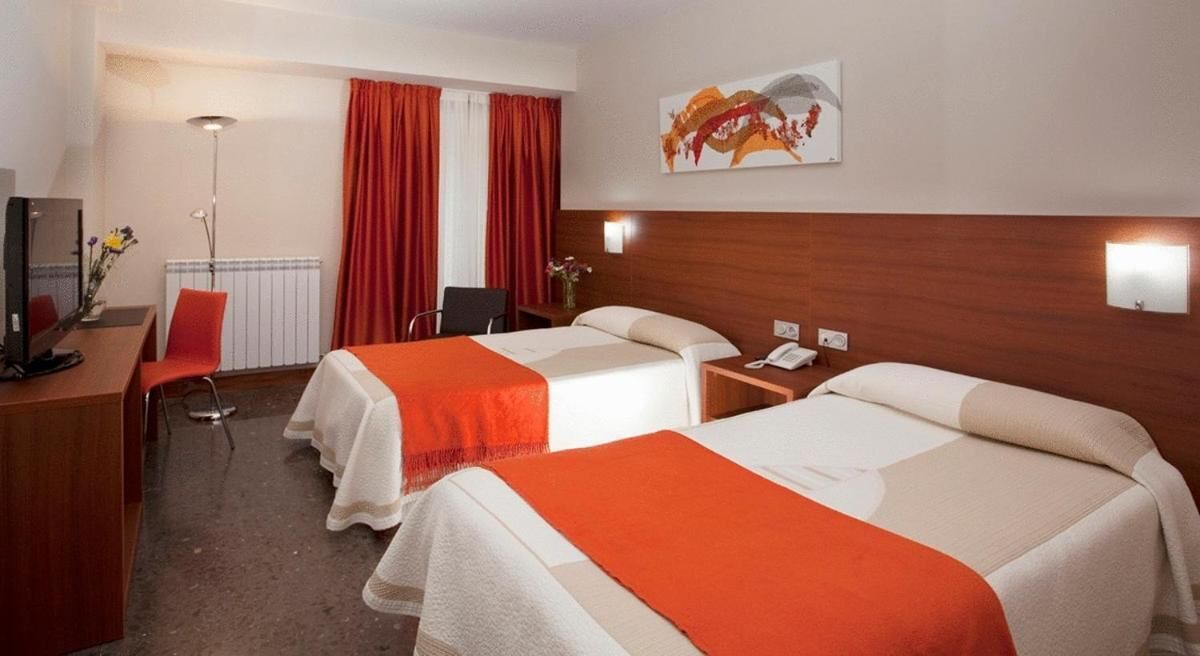 Habitación de hotel con dos camas, un escritorio, una silla, un televisor y un cuadro en la pared.
