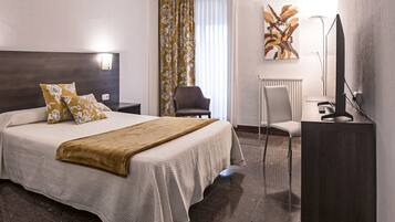 A hotel room with a large bed, a desk, a chair, a TV, and a radiator.