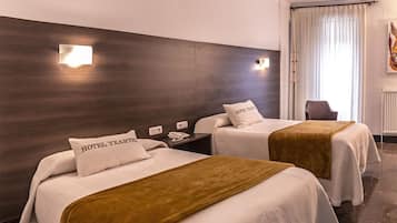Habitación de hotel con dos camas, cada una con un cojín que dice "HOTEL TXARTEN". Hay apliques en la pared y una silla en la esquina.