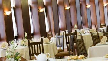 A restaurant with multiple tables set for dining, each with white tablecloths and wooden chairs.