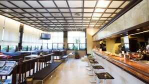 Um restaurante espaçoso com tetos altos, grandes janelas e um balcão comprido com bancos.