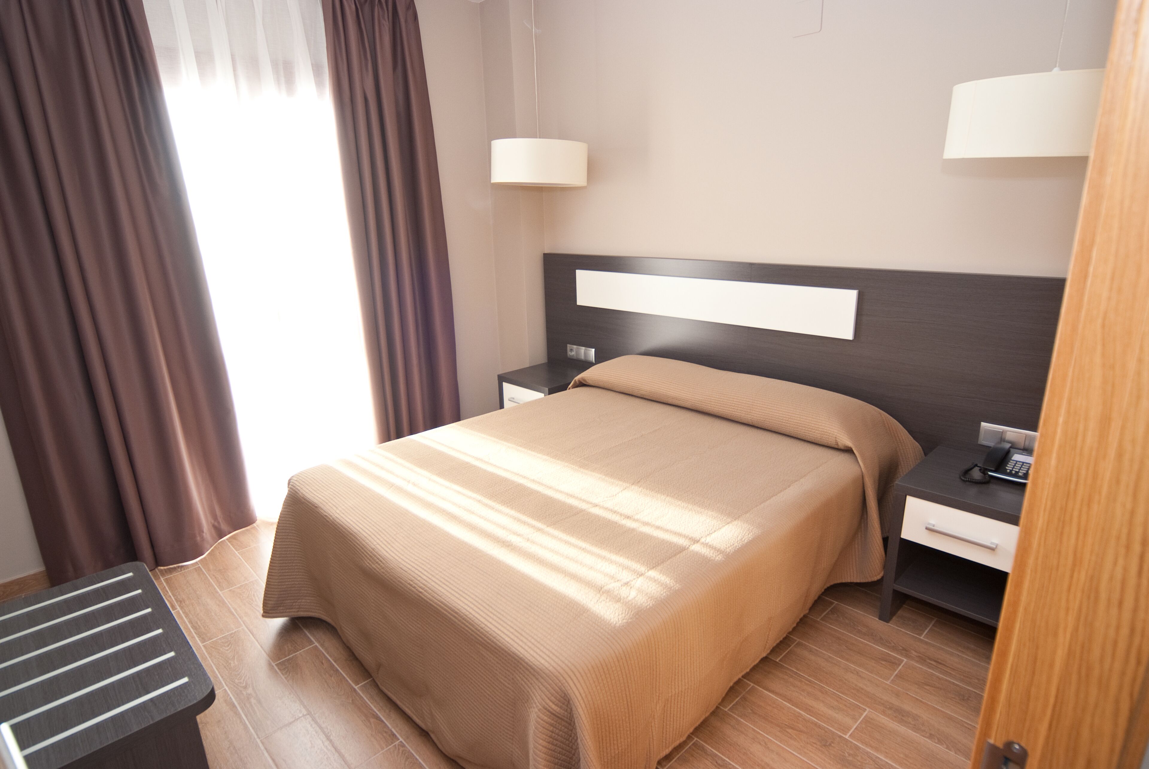 Une chambre d’hôtel bien rangée, avec un grand lit, des tables de chevet et une petite table de nuit avec une lampe.