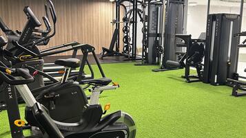 A gym with various exercise equipment, including treadmills and weight machines, on a green artificial turf floor.