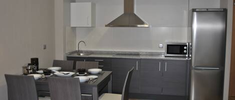 A compact kitchen with dark cabinets, a stainless steel refrigerator, a microwave, and a dining area with chairs and a table set for four.