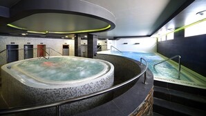 Una piscina interna moderna con idromassaggio, immersa in pareti scure e un soffitto curvo.