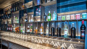 Un'area bar con scaffali pieni di bottiglie di liquori e una fila di bicchieri da vino vuoti.