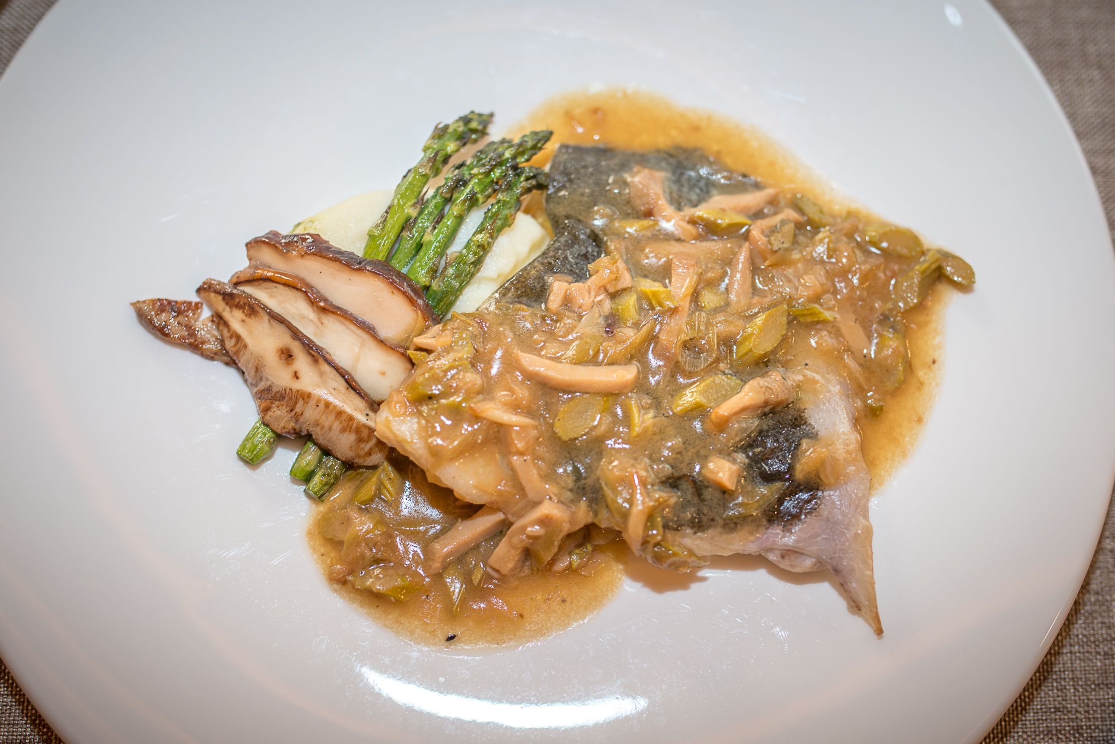 Plat de menjar amb una secció de peix, espàrrecs i salsa cremosa.