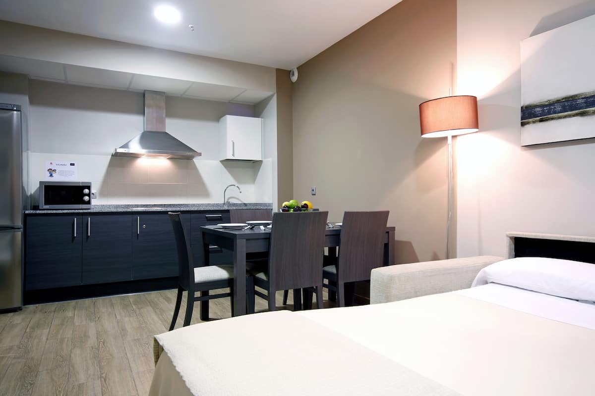 A compact hotel room with a kitchenette, a dining area, and a bed.