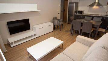 Una sala de estar moderna con una televisión de pantalla plana, un sofá blanco, una mesa de centro y un comedor con una mesa y sillas.