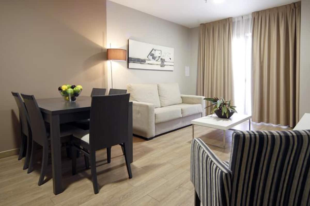 A modern living room with a dining area, a sofa, a striped armchair, a coffee table, and a lamp.