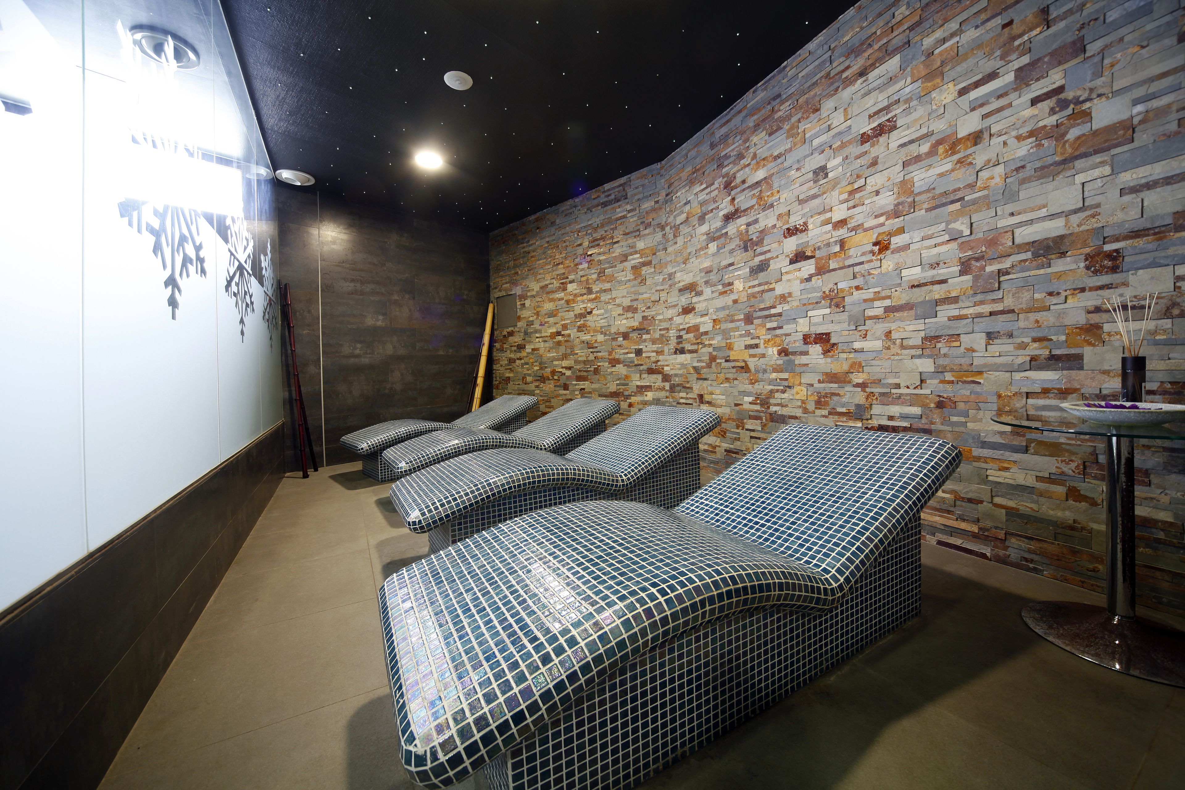 Une salle de spa avec un mur en pierre, une table de massage et une petite table sur laquelle est posé un vase.