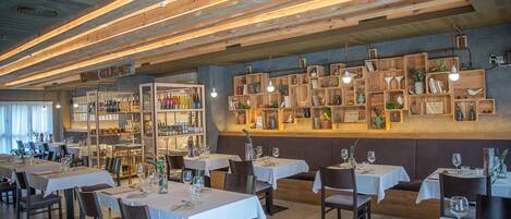 A restaurant interior with wooden ceiling beams, white tablecloths, and shelves with various items.