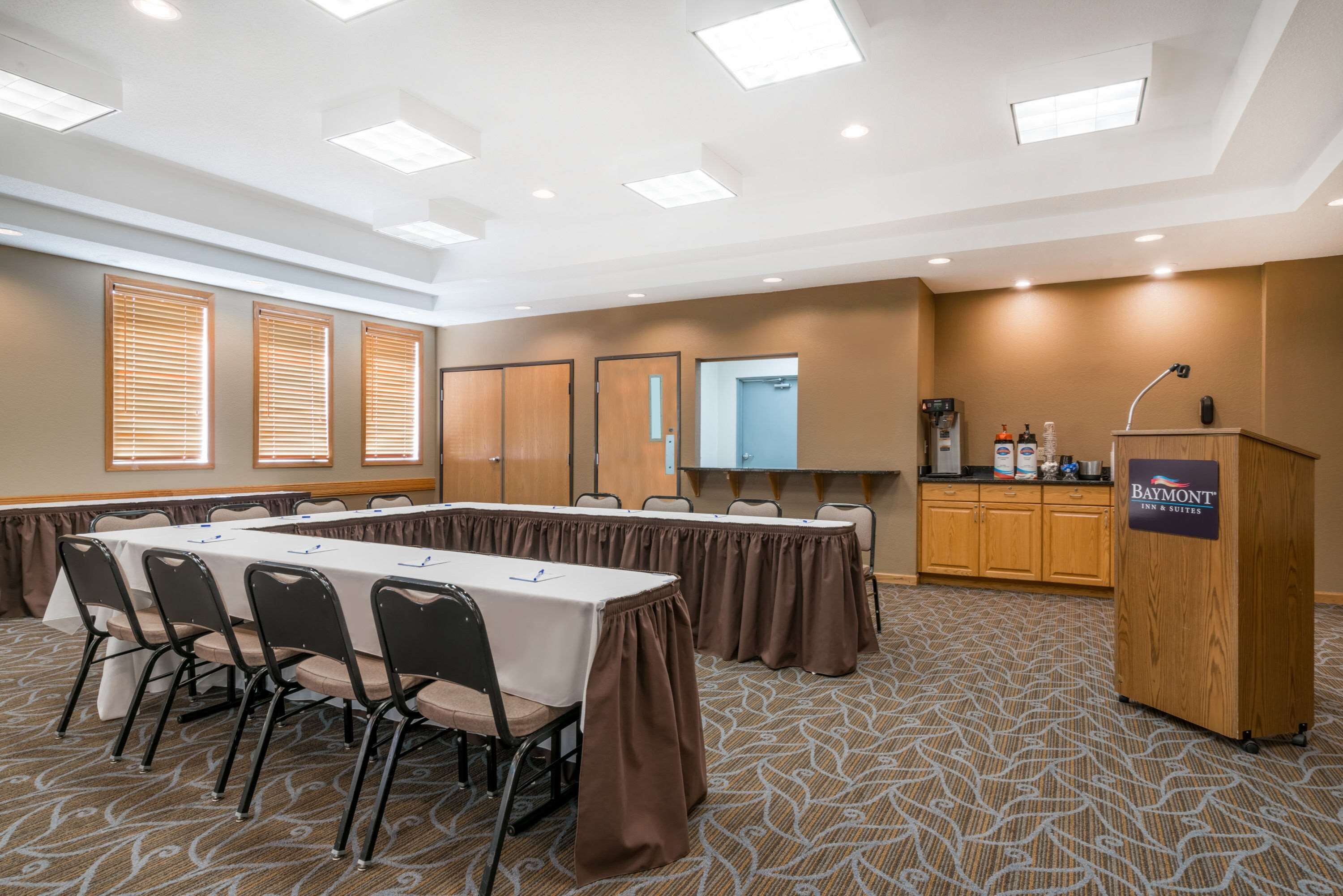 A conference room with a long table, chairs, a podium, and a kitchenette area.