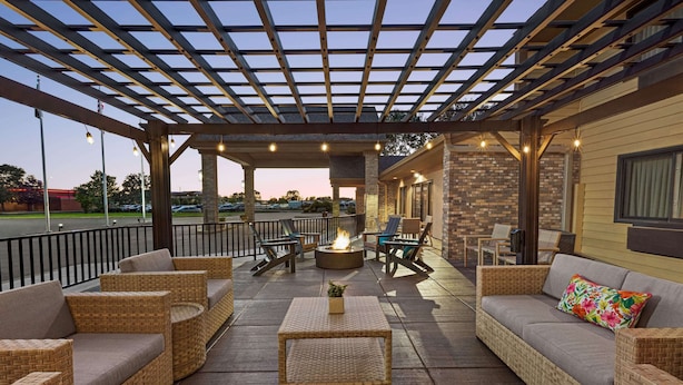 Un espace extérieur aménagé en terrasse, avec des meubles en osier, un foyer et une pergola illuminée de guirlandes lumineuses.