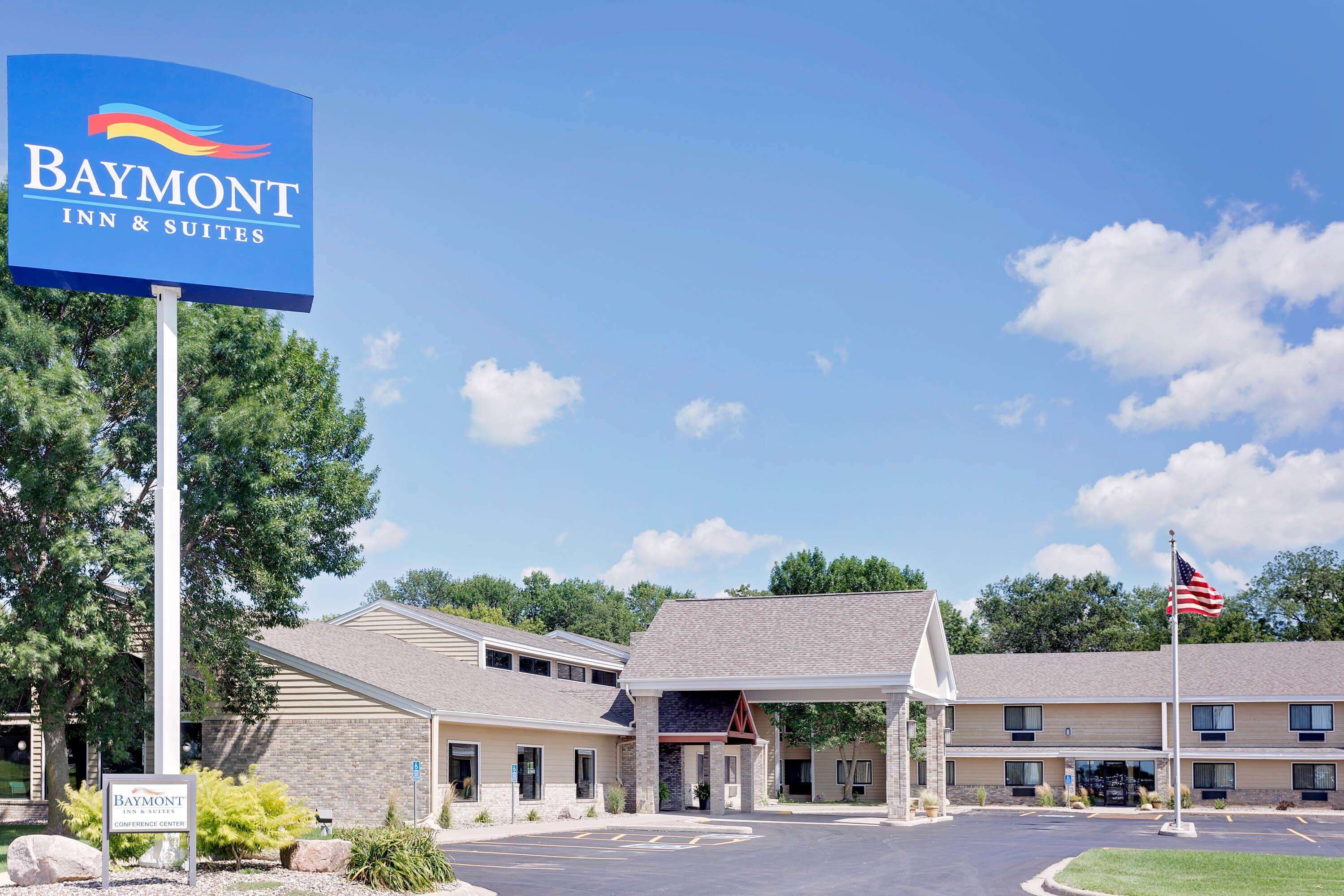 A Baymont Inn & Suites building with a parking lot, a covered entrance, and an American flag.