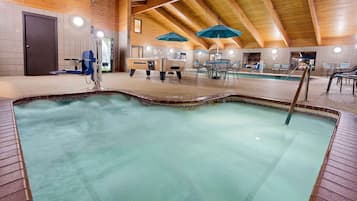 An indoor swimming pool with a wooden ceiling, a changing room, and a seating area with umbrellas.