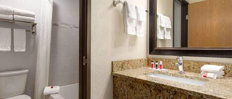 A bathroom with a toilet, shower, sink, and mirror.
