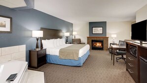 Une chambre d’hôtel avec un grand lit, un bureau avec une chaise, une télévision, une cheminée et une salle de bain équipée d’une baignoire et de toilettes.