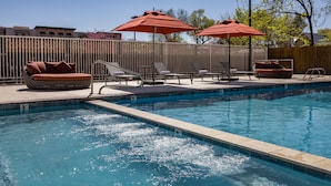 A swimming pool with lounge chairs and umbrellas, surrounded by a fence. - River Canyon Lodge (Moab)