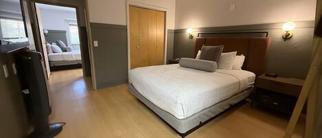 A bedroom with a bed, bedside tables, a wardrobe, and a door leading to another room.