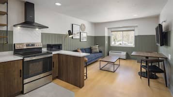 A modern kitchen with a built-in oven, a dining area with a table and chairs, a sofa, and a window providing natural light.