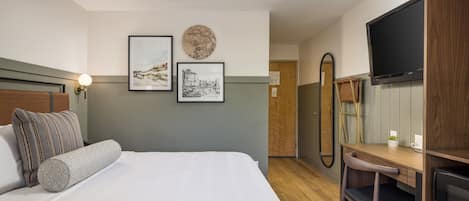 A hotel room with a bed, a desk, a chair, a television, and artwork on the walls.