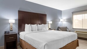 Une chambre d’hôtel avec un grand lit, deux tables de chevet avec des lampes, une chaise et une fenêtre avec des stores.