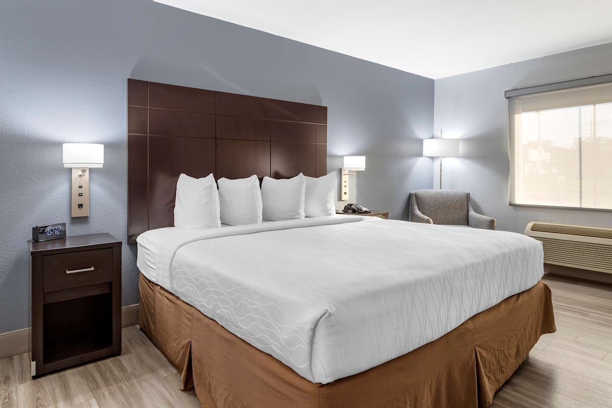 A hotel room with a large bed, two bedside tables with lamps, a chair, and a window with blinds.